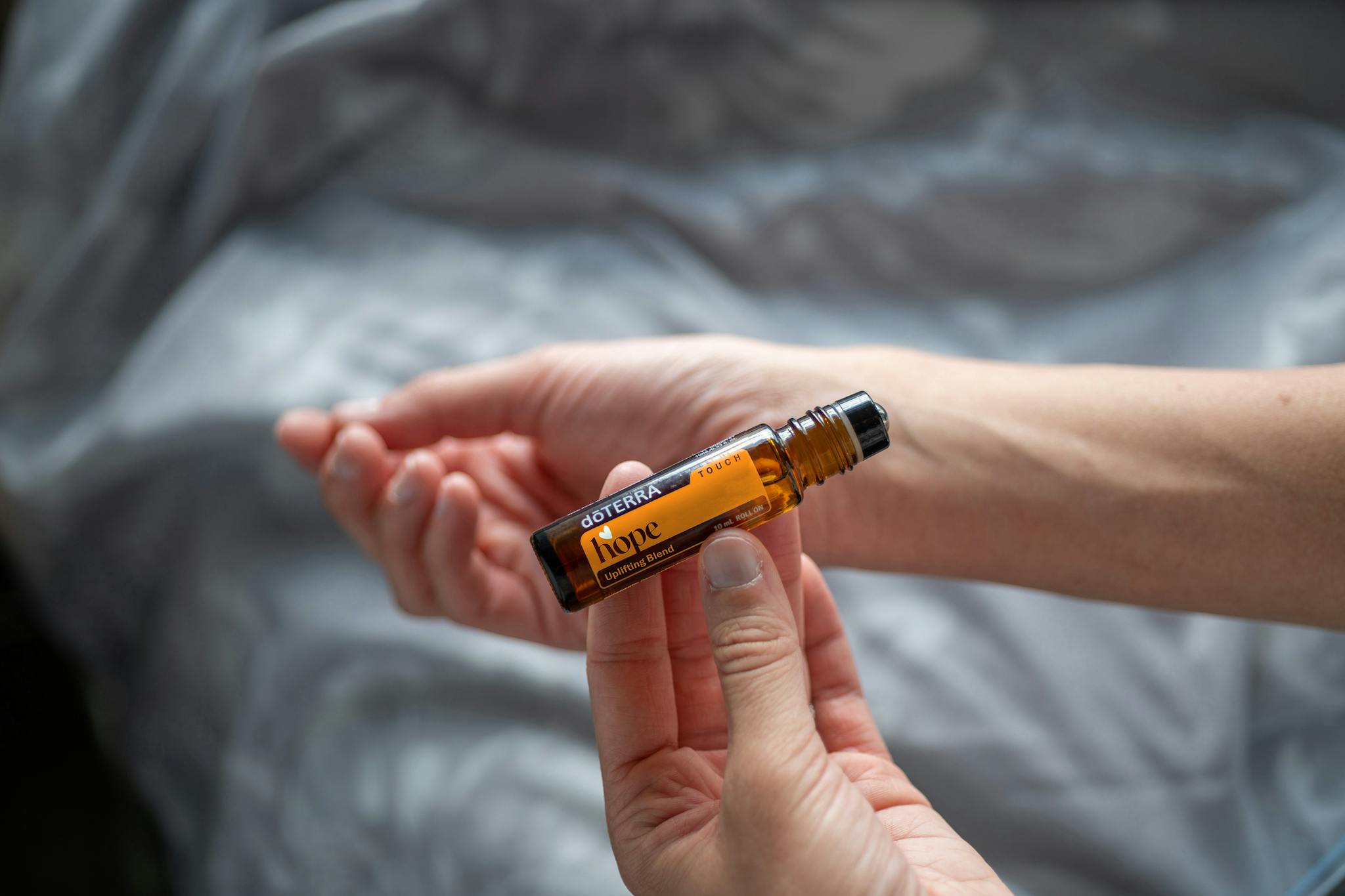 A close-up of hands holding a brown essential oil bottle labeled 'Hope' against a neutral background.