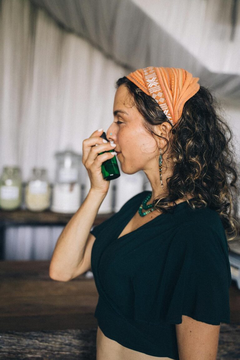 Woman smelling essential oil bottle indoors, conveying relaxation and wellness.